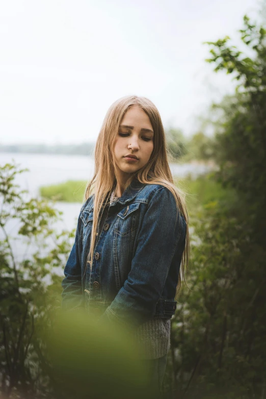 a woman standing in front of a body of water, a picture, inspired by Elsa Bleda, unsplash, renaissance, wearing a jeans jackets, pouty face, blonde swedish woman, 1 6 years old
