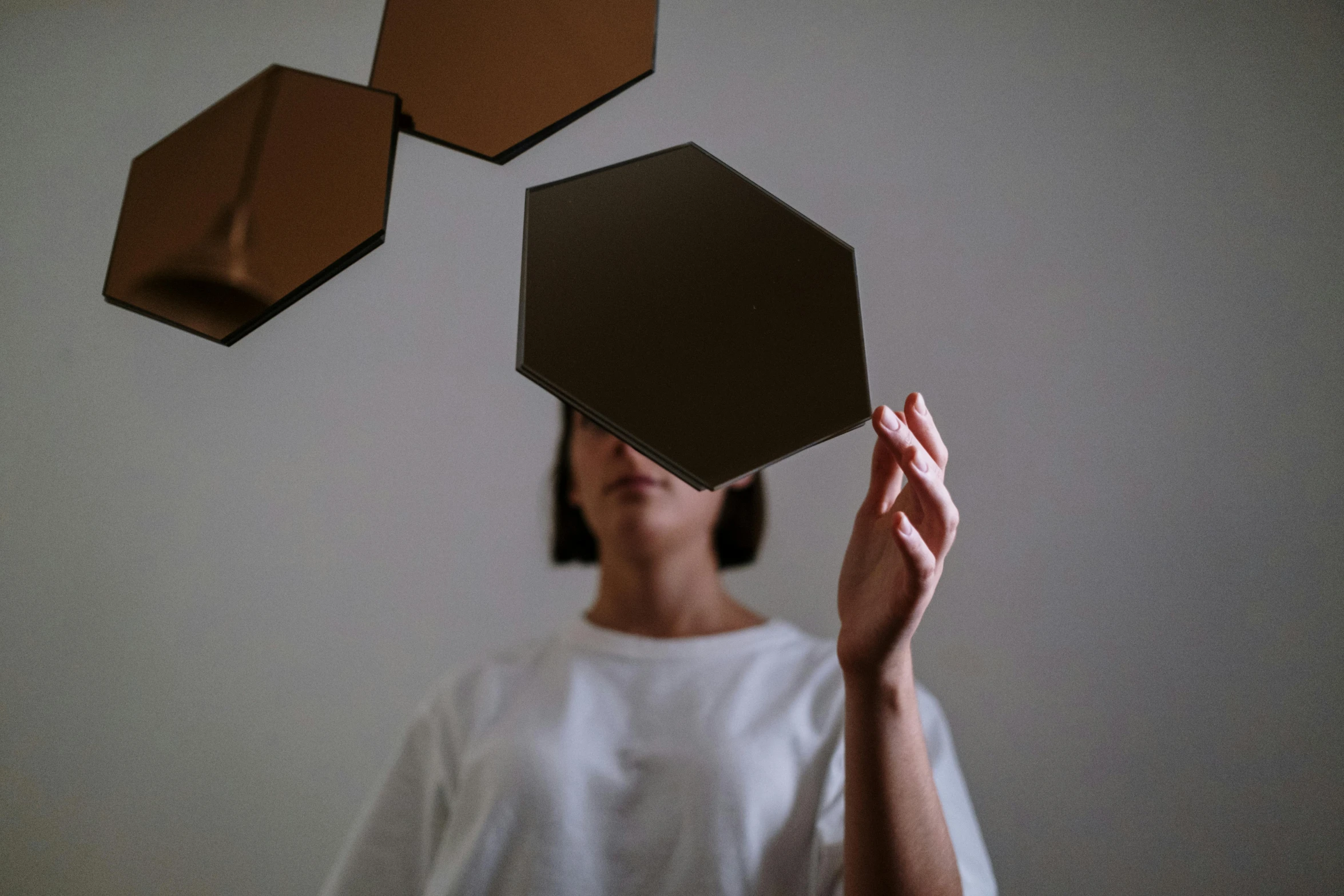 a woman holding a mirror in front of her face, an abstract sculpture, inspired by Anna Füssli, unsplash contest winner, kinetic art, hexagons, black and auburn colour pallet, hovering indecision, chocolate