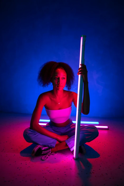 a woman sitting on the ground holding a pole, by Emanuel Witz, light and space, doja cat, neon colors, body full glowing vacuum tubes, low saturated red and blue light