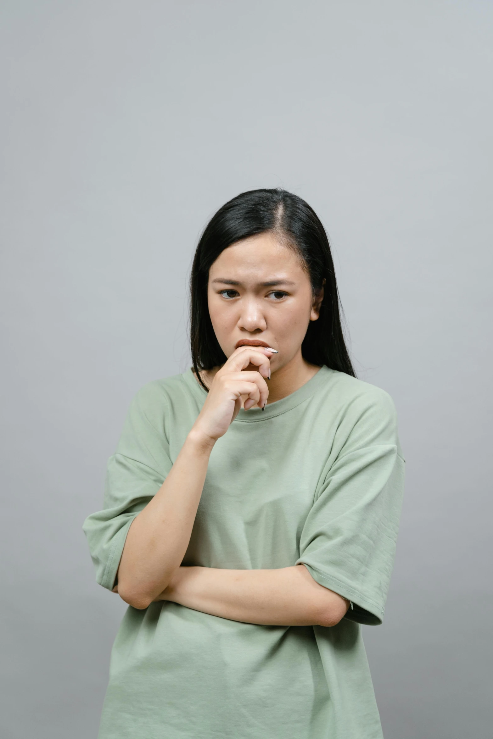 a woman in a green shirt is holding her hand to her mouth, inspired by Zhang Kechun, trending on pexels, realism, grey backdrop, worried, thoughtful ), distraught