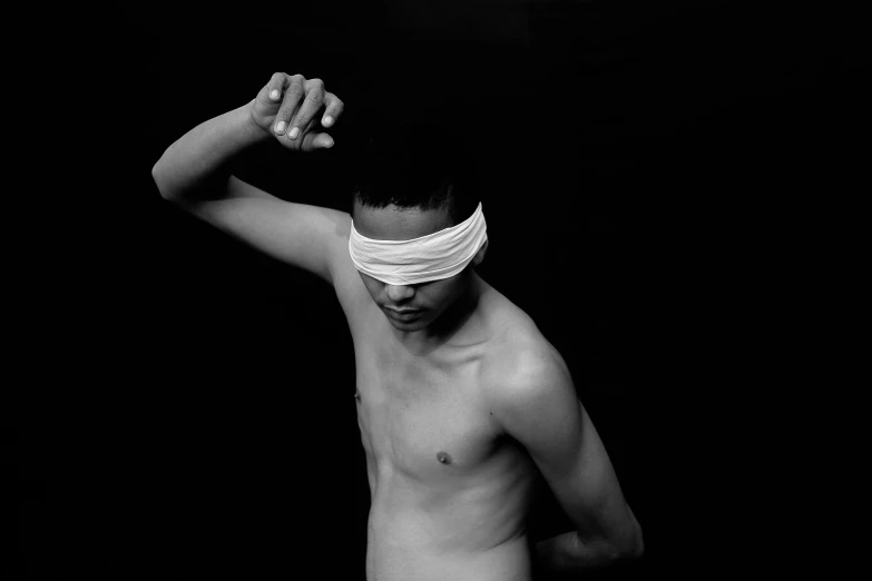 a black and white photo of a man with a blindfold, an album cover, inspired by Robert Mapplethorpe, unsplash, black teenage boy, disrobed, white bandages on fists, pointè pose