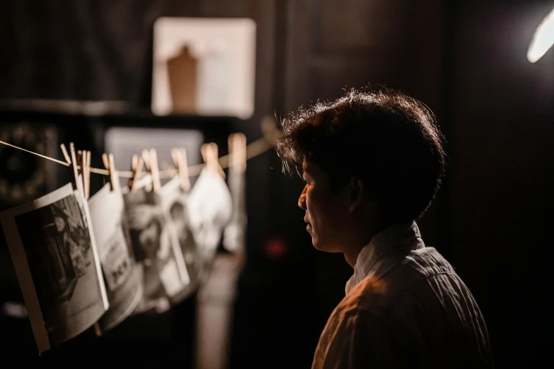 a boy looking at pictures hanging on a clothes line, pexels contest winner, visual art, group of people in a dark room, an asian woman, profile image, taken in the early 2020s