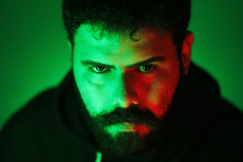 a close up of a man with a beard, an album cover, inspired by Elsa Bleda, pexels, serial art, glowing green neon eyes, arab man light beard, menacing pose, film still from a horror movie