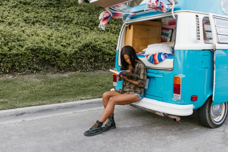 a woman sitting in the back of a van reading a book, pexels contest winner, wearing denim short shorts, avatar image, an olive skinned, jean and multicolor shoes