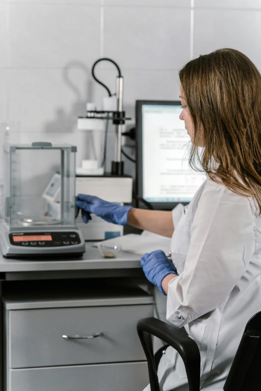 a woman sitting at a desk in front of a computer, handling laboratory equipment, immaculate scale, thumbnail, grey