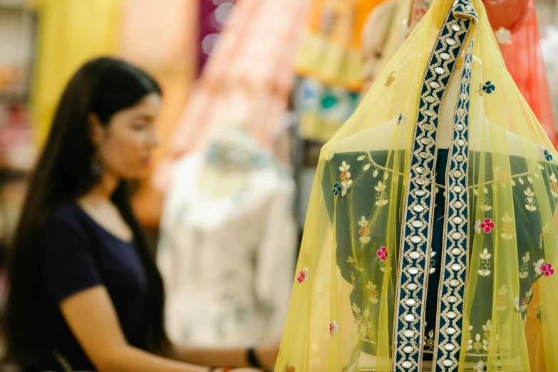 a woman is shopping in a clothing store, trending on unsplash, hurufiyya, neon yellow madhubani, medium close shot, south east asian with long, veils and jewels