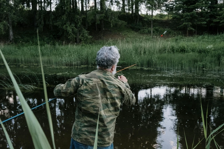a man that is standing in the water with a fishing rod, near forest, facing away from the camera, an oldman, attacking