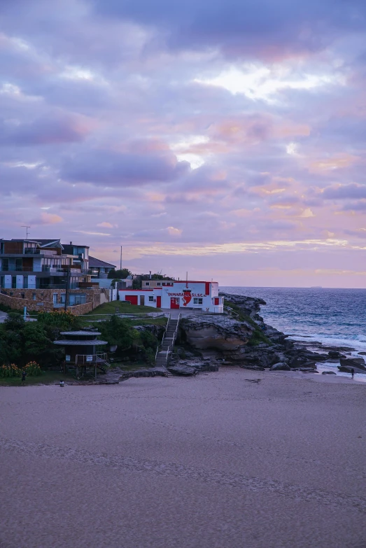 a couple of benches sitting on top of a sandy beach, a matte painting, unsplash, bondi beach in the background, cliff side at dusk, purple roofs, fishing village