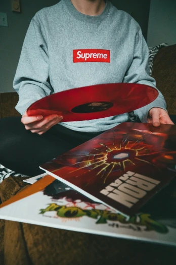 a man sitting on a couch holding a red vinyl record, an album cover, inspired by Elsa Bleda, featured on reddit, supreme pizza, headbang till your brain bleeds, inspect in inventory image, supreme