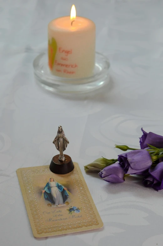 a candle and some purple flowers on a table, virgin mary, opal statues, birdseye view, mini model