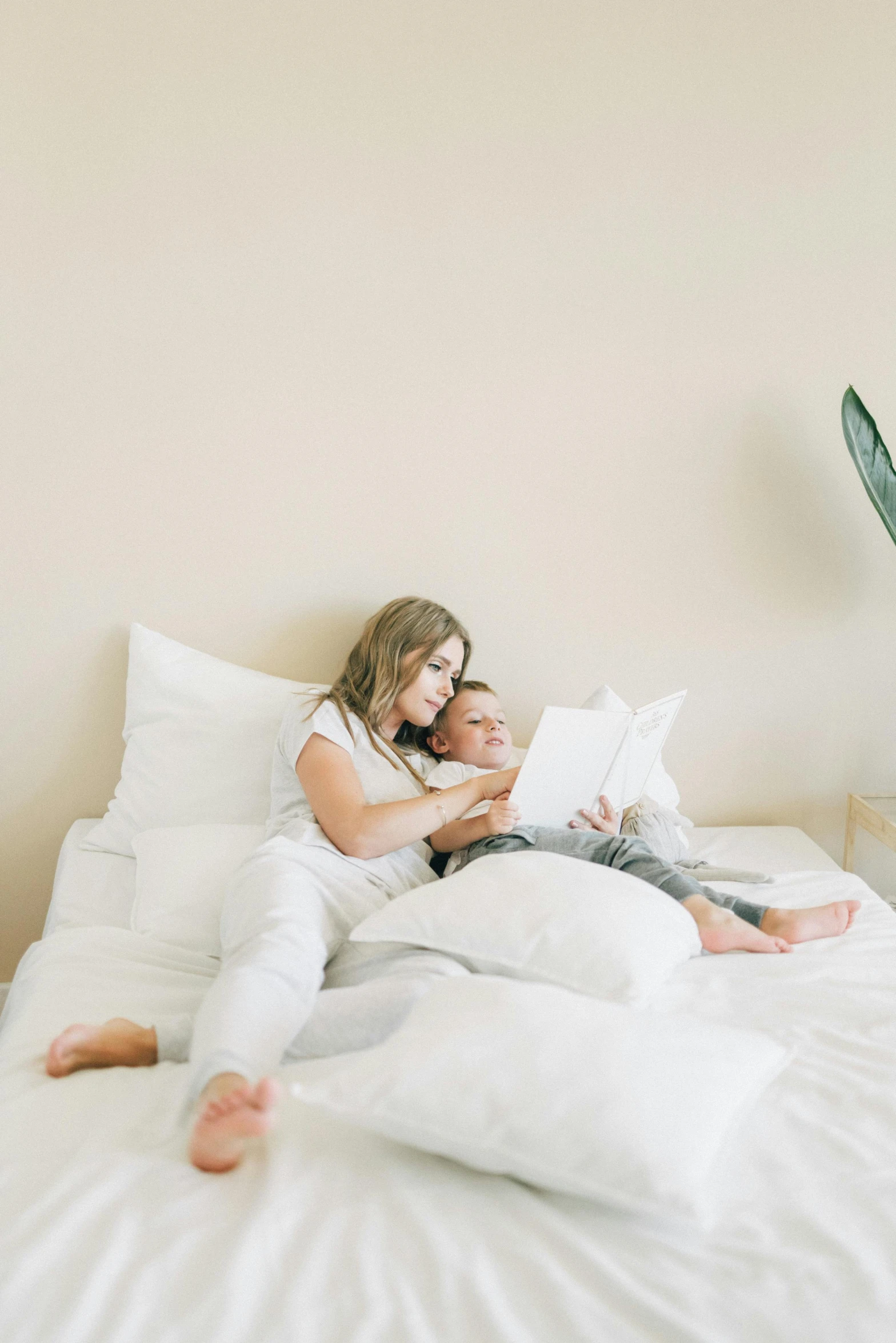 a man and a woman laying on a bed, by Nicolette Macnamara, pexels contest winner, white pillows, reading the book about love, motherly, with a white background