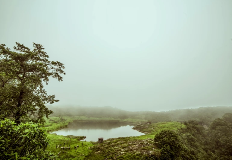 a body of water sitting on top of a lush green hillside, an album cover, pexels contest winner, hurufiyya, foggy weather atmosphere, india, near pond, analog photo