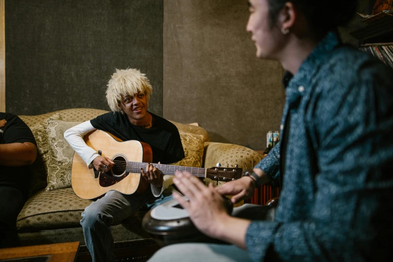 a man sitting on a couch playing a guitar, unsplash, fiona staples and kinu nishimura, short blonde afro, talking, practice