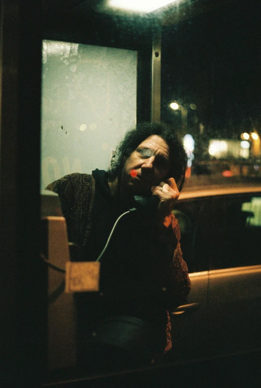 a man sitting at a bus stop talking on a cell phone, an album cover, inspired by Nan Goldin, pexels, clown, leatherface, nighttime, fujicolor superia photo