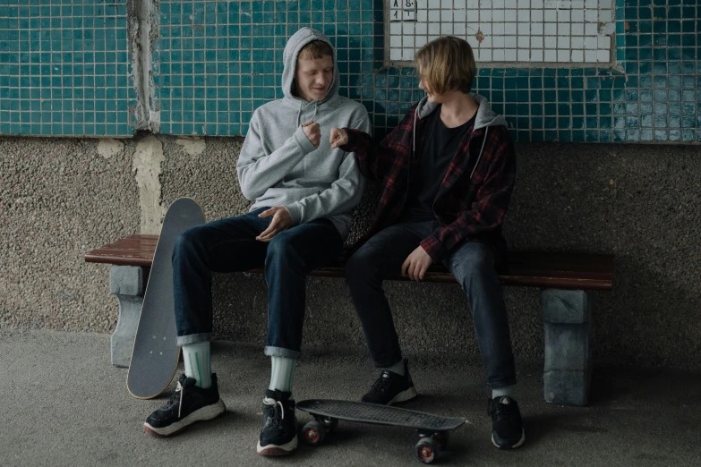 two people sitting on a bench with skateboards, by Emma Andijewska, teenage boy, promo still, boys, lightweight