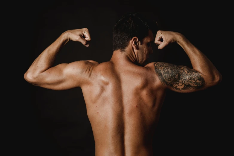 a man flexing his muscles against a black background, a tattoo, pexels contest winner, arched back, plain background, mesomorph, back to back