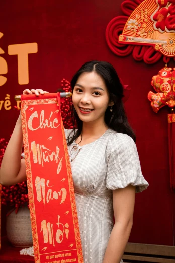 a woman holding a red sign in front of a red wall, inspired by Cui Bai, in style of lam manh, ribbon, 1 8 yo, commercial banner