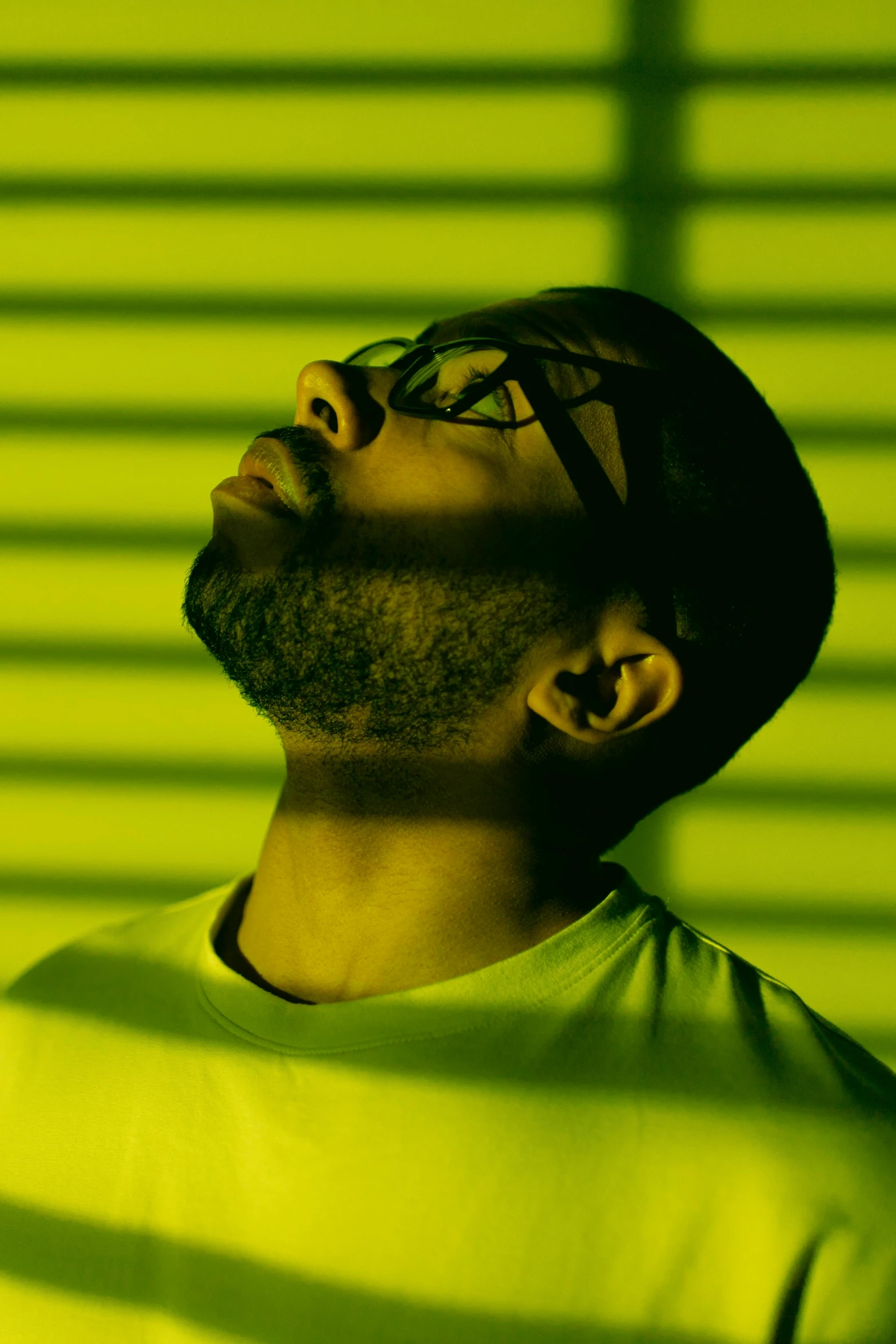 a man standing in front of a green wall, an album cover, inspired by Agnolo Gaddi, trending on pexels, yellow lighting from right, man with glasses, drake, eyes closed