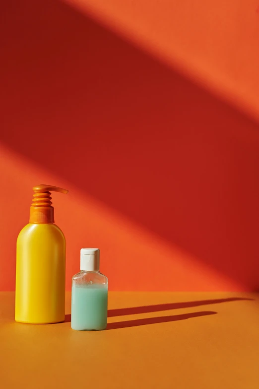 a bottle of hand sanitizer next to a bottle of hand sanitizer, a still life, trending on pexels, plasticien, in front of an orange background, thinning hair, red and teal and yellow, synthetic materials