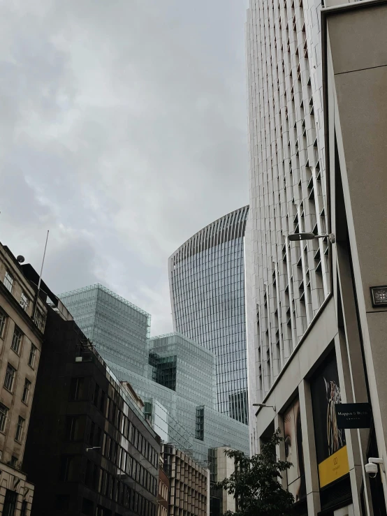 a group of people walking down a street next to tall buildings, grey skies, buildings made out of glass, london, low quality photo