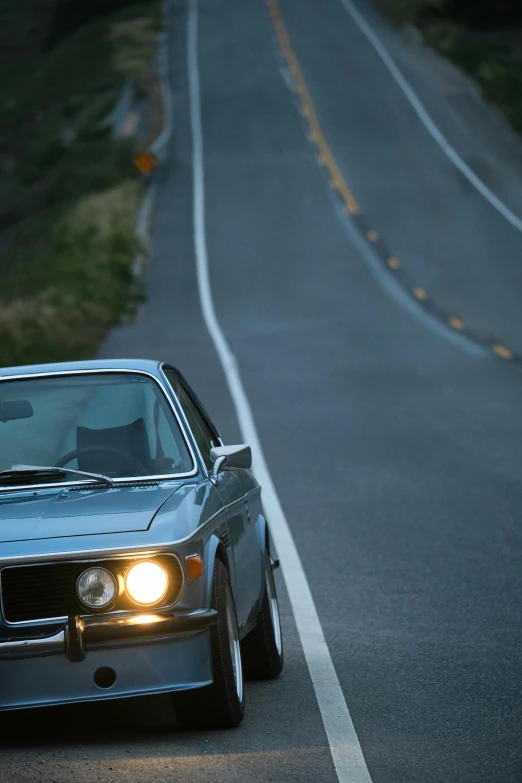 a silver car driving down a curvy road, an album cover, unsplash, photorealism, blue headlights, 1979, bmw, stephen shore