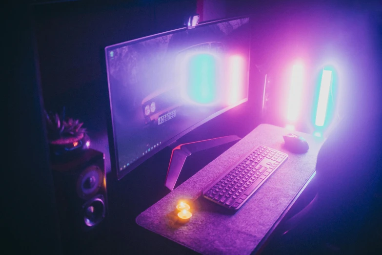 a computer desk with a keyboard, mouse and monitor, inspired by Beeple, pexels, purple color lighting, rainbow lighting, dusty lighting, purple and pink