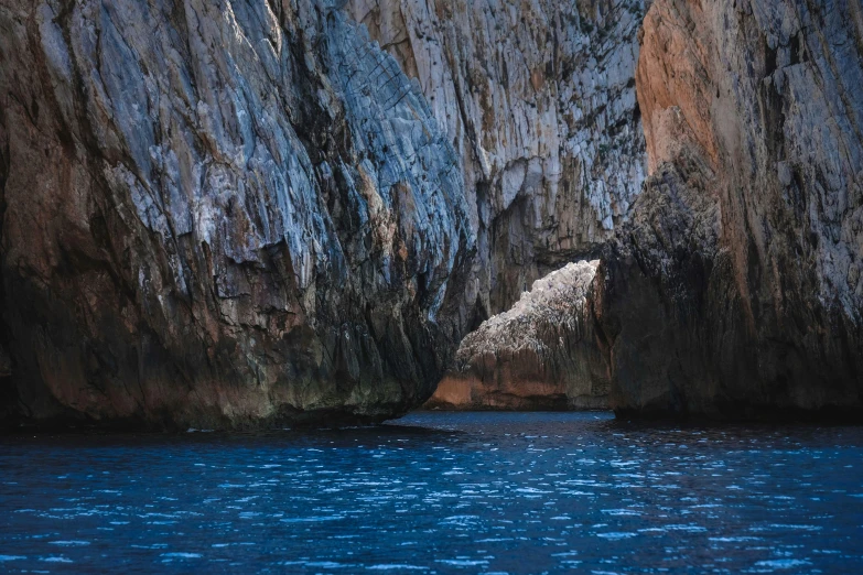 a large rock formation in the middle of a body of water, inspired by Fede Galizia, pexels contest winner, romanticism, dark blue water, slim aarons, grotto, thumbnail