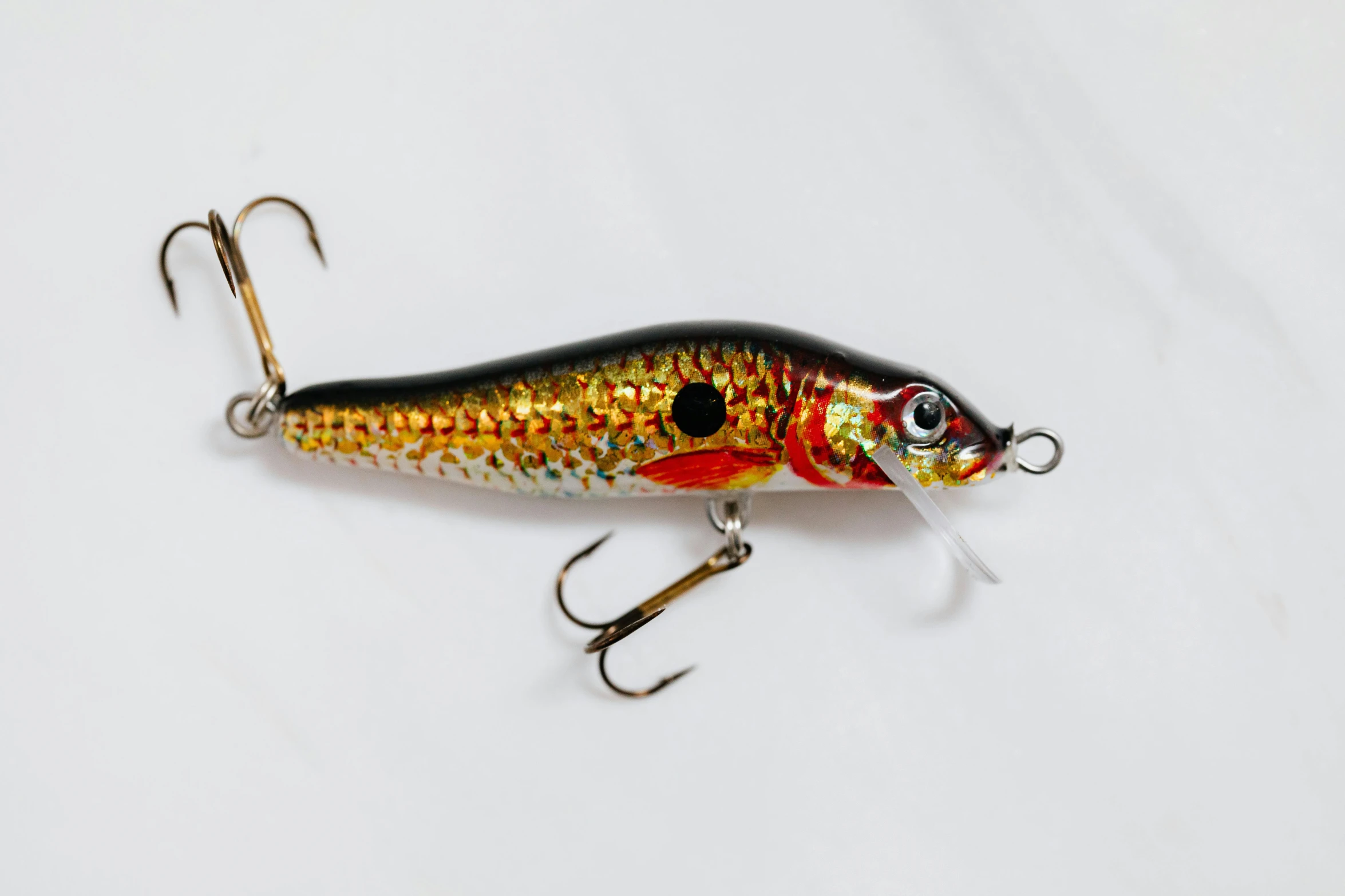 a close up of a lure on a white surface, trending on pexels, golden rainbow tubing, in style of ultra realistic, wooden, shining gold and black and red