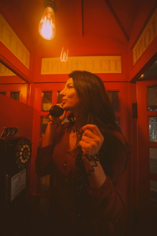 a woman talking on a cell phone in a room, inspired by Elsa Bleda, pexels contest winner, art nouveau, red lights, bells, jukebox, shohreh aghdashloo