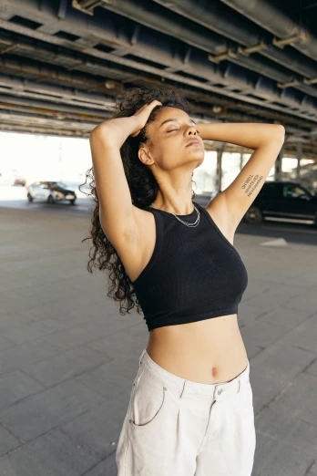 a beautiful young woman standing under a bridge, trending on pexels, renaissance, wearing a cropped black tank top, on a parking lot, relaxed posture, mixed-race woman