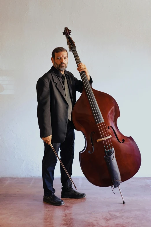 a man standing next to a double bass, inspired by Cándido López, press shot, rectangle, backdrop, profile image