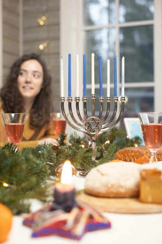 a woman sitting at a table with a menorah in front of her, holiday season, vine, taken in 2 0 2 0, caspar david