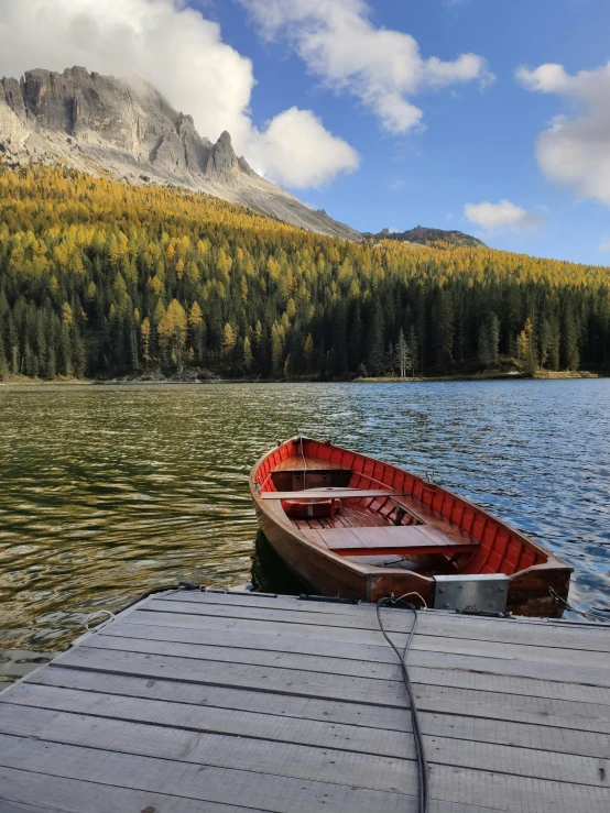 a boat sitting on top of a wooden dock next to a lake, in the dolomites, slide show, cute photo