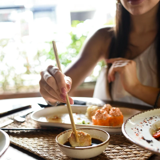 a woman sitting at a table with plates of food, unsplash, chopsticks, holding a wooden staff, trending photo, single subject