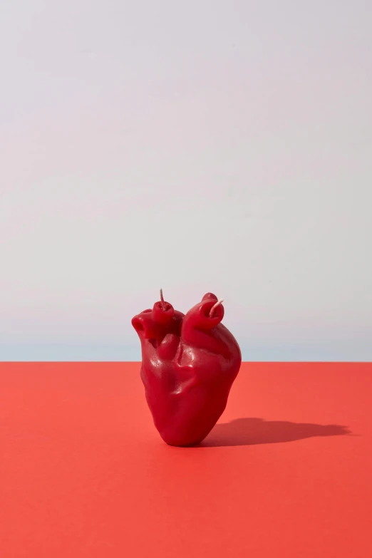 a red heart shaped object on a red surface, a surrealist sculpture, unsplash, photorealism, waxy candles, 3/4 front view, dwell, made of glazed