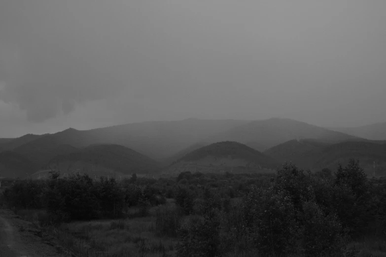 a black and white photo of a dirt road, a black and white photo, unsplash, tonalism, distant town in valley and hills, rainy evening, ! apocalypse landscape!!, the photo was taken from afar