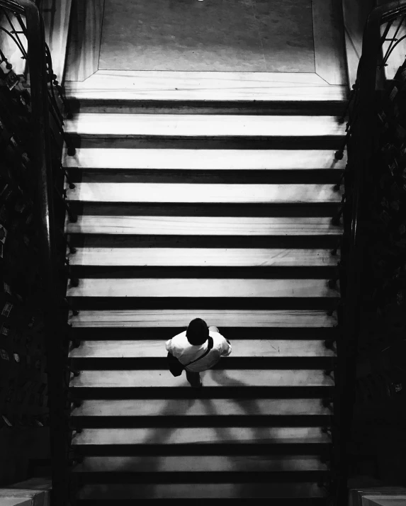a black and white photo of a person sitting on a set of stairs, inspired by Arnold Newman, unsplash, top down view, ffffound, silhouette of man, in a museum