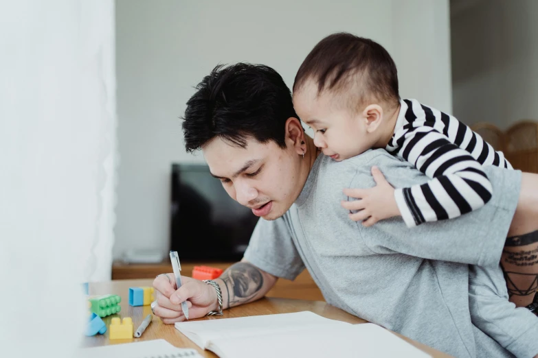 a man holding a baby and writing on a piece of paper, a child's drawing, pexels contest winner, avatar image, asian male, attractive photo, stacked image