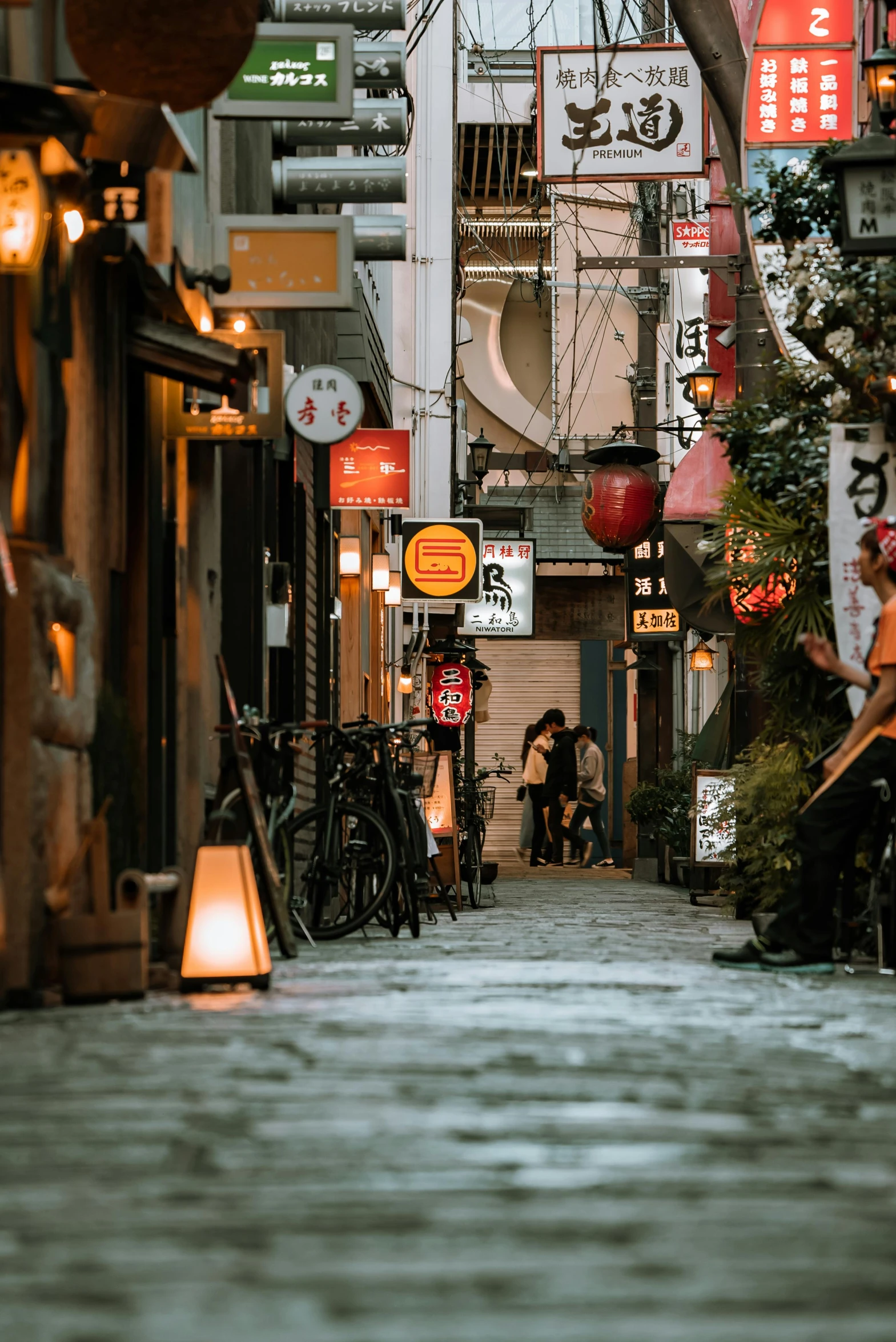 a person sitting on a bench in a narrow alley, by Julia Pishtar, pexels contest winner, ukiyo-e, lamps on ground, tokyo izakaya scene, cobblestone streets, ethnicity : japanese