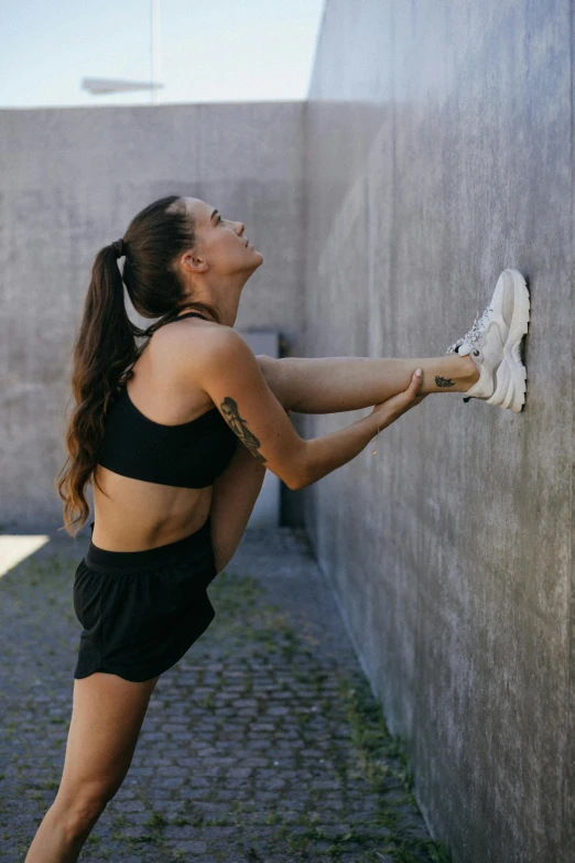 a woman stretching in front of a wall, wearing black shorts, with a ponytail, well edited, laced