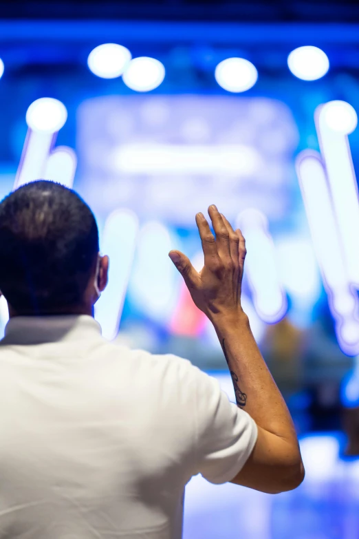 a man standing in front of a stage with his hands in the air, pray, interrupting the big game, in sao paulo, bokeh”