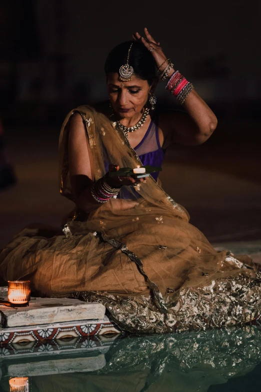 a woman in a sari sitting next to a pool, pexels contest winner, renaissance, lit with candles, holding a tattered magical book, performing on stage, intricate led jewellery