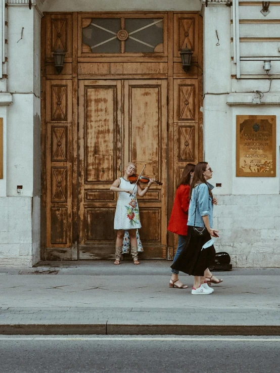 a group of people standing in front of a wooden door, by Emma Andijewska, pexels contest winner, neoclassicism, violin, summer street, view from the streets, square