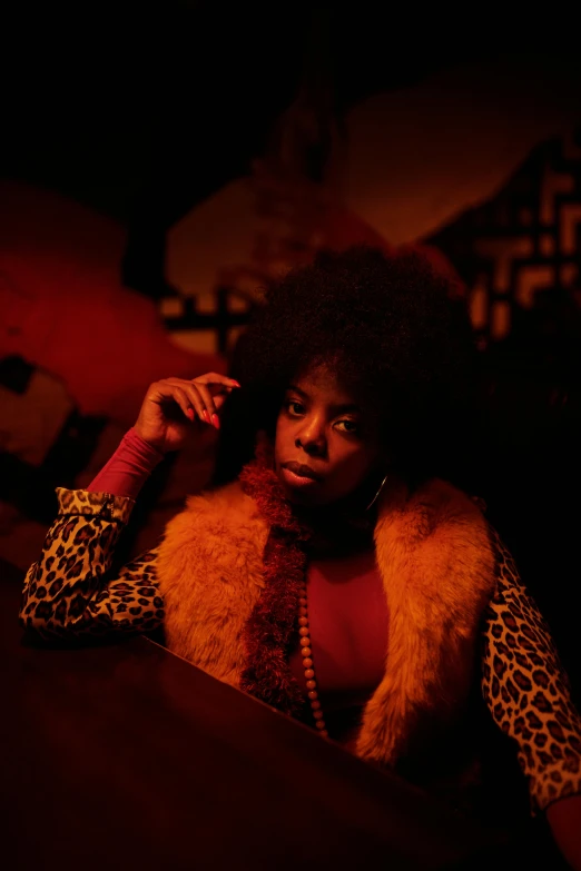 a woman sitting at a table talking on a cell phone, an album cover, pexels, funk art, yellow fur, in a dark dusty parlor, afro, crimson