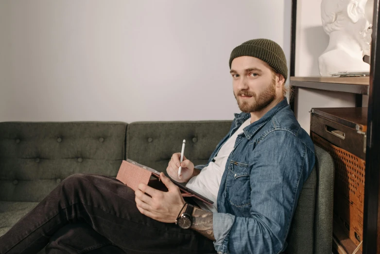 a man sitting on a couch smoking a cigarette, inspired by Seb McKinnon, trending on pexels, holding notebook, avatar image, caracter with brown hat, sketching