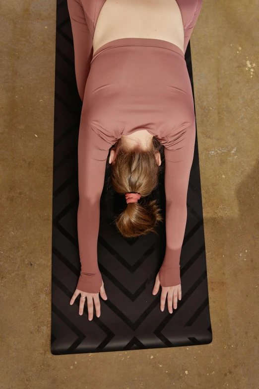 a woman doing a yoga pose on a mat, by Rachel Reckitt, top down shot, black and terracotta, back towards camera, arm