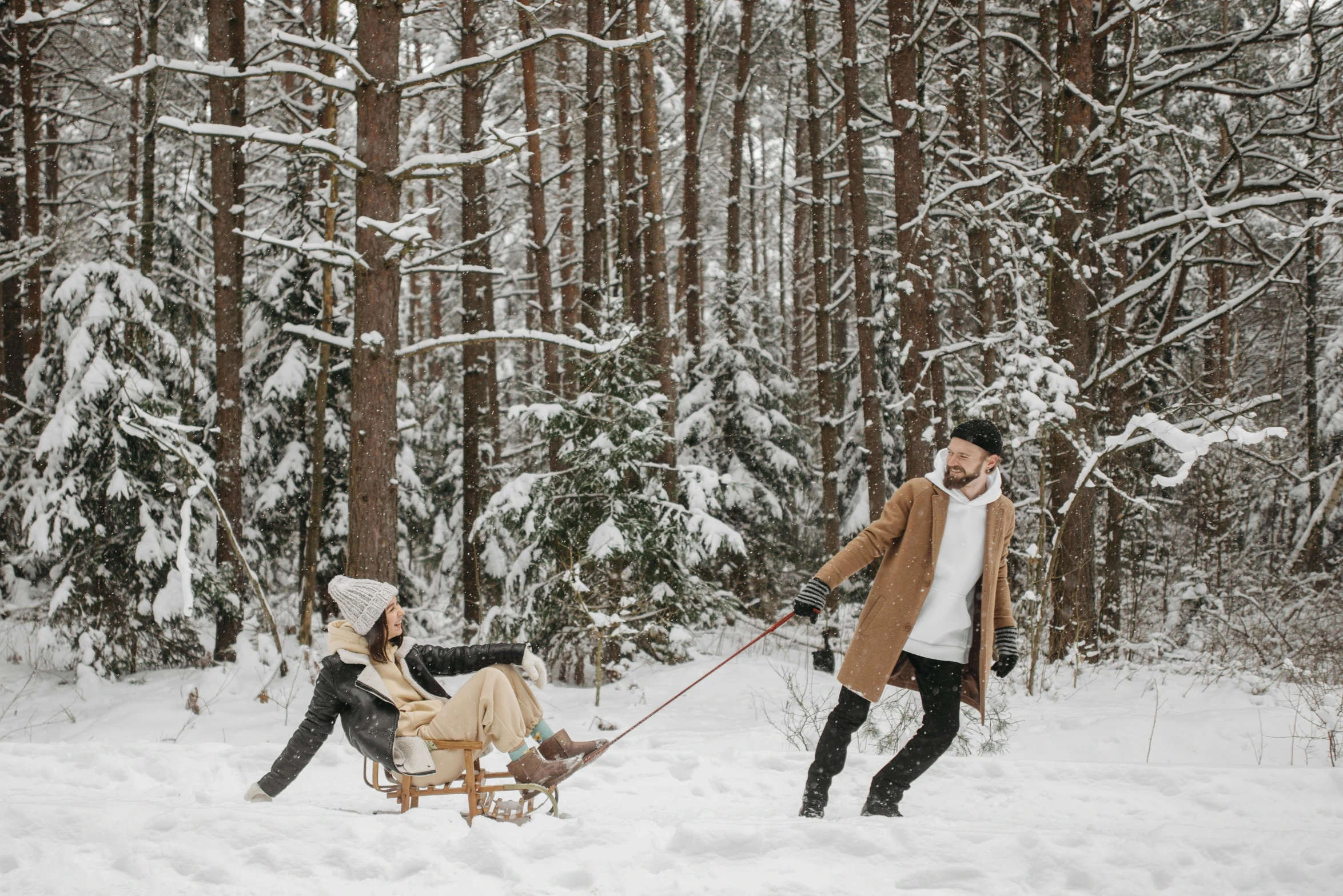 a man pulling a child on a sled in the snow, by Emma Andijewska, pexels contest winner, renaissance, forest picnic, avatar image, couple, in style of joel meyerowitz