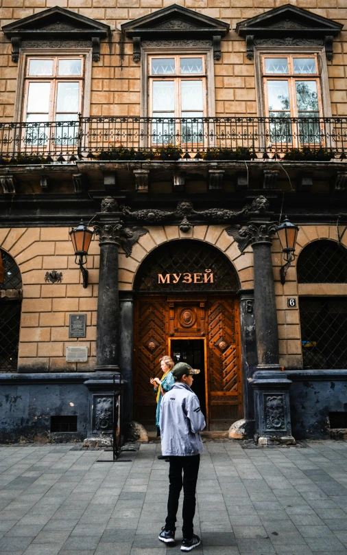 a man standing in front of a large building, by Miroslava Sviridova, pexels contest winner, art nouveau, tavern, woman holding another woman, ukraine. professional photo, 15081959 21121991 01012000 4k