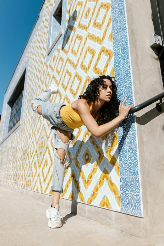 a woman leaning against the side of a building, trending on pexels, arabesque, breakdancing, inside a frame on a tiled wall, wearing yellow croptop, hollywood promotional image