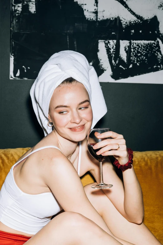 a woman sitting on a couch holding a glass of wine, a portrait, inspired by Elsa Bleda, trending on pexels, wearing a towel, over it's head, eleanor tomlinson, nightlife